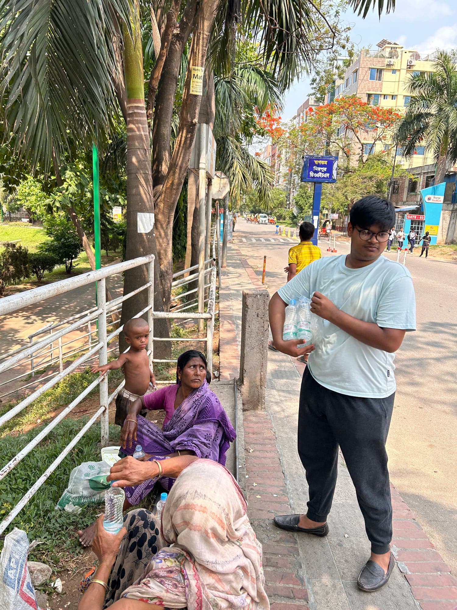 A volunteer carrying bottled water to women resting beside a Mirpur road