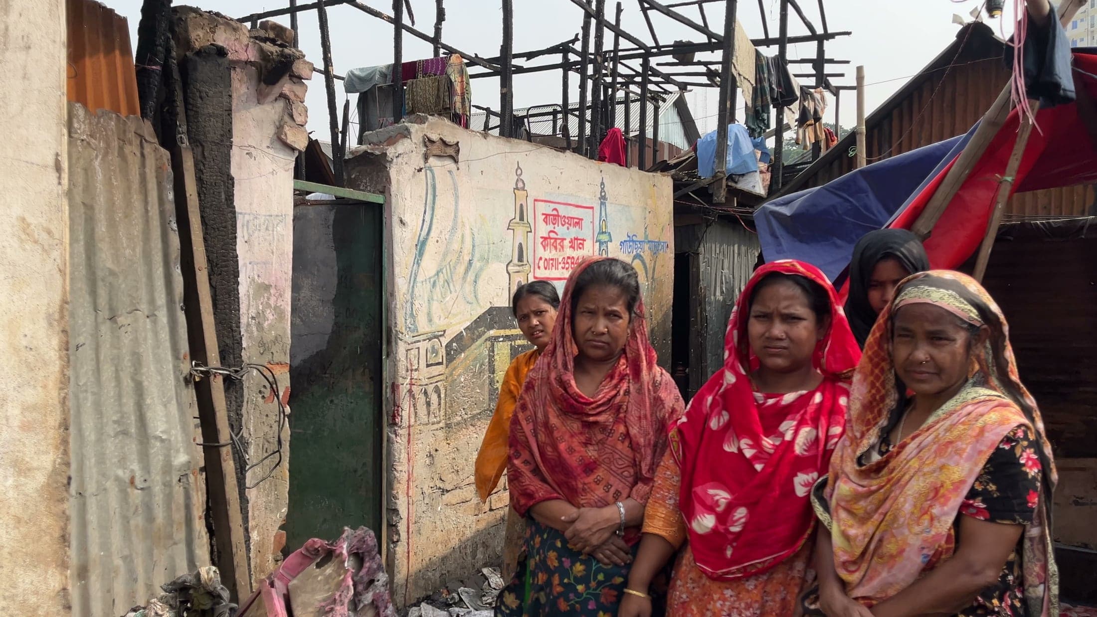 Korail residents standing beside fire-damaged homes
