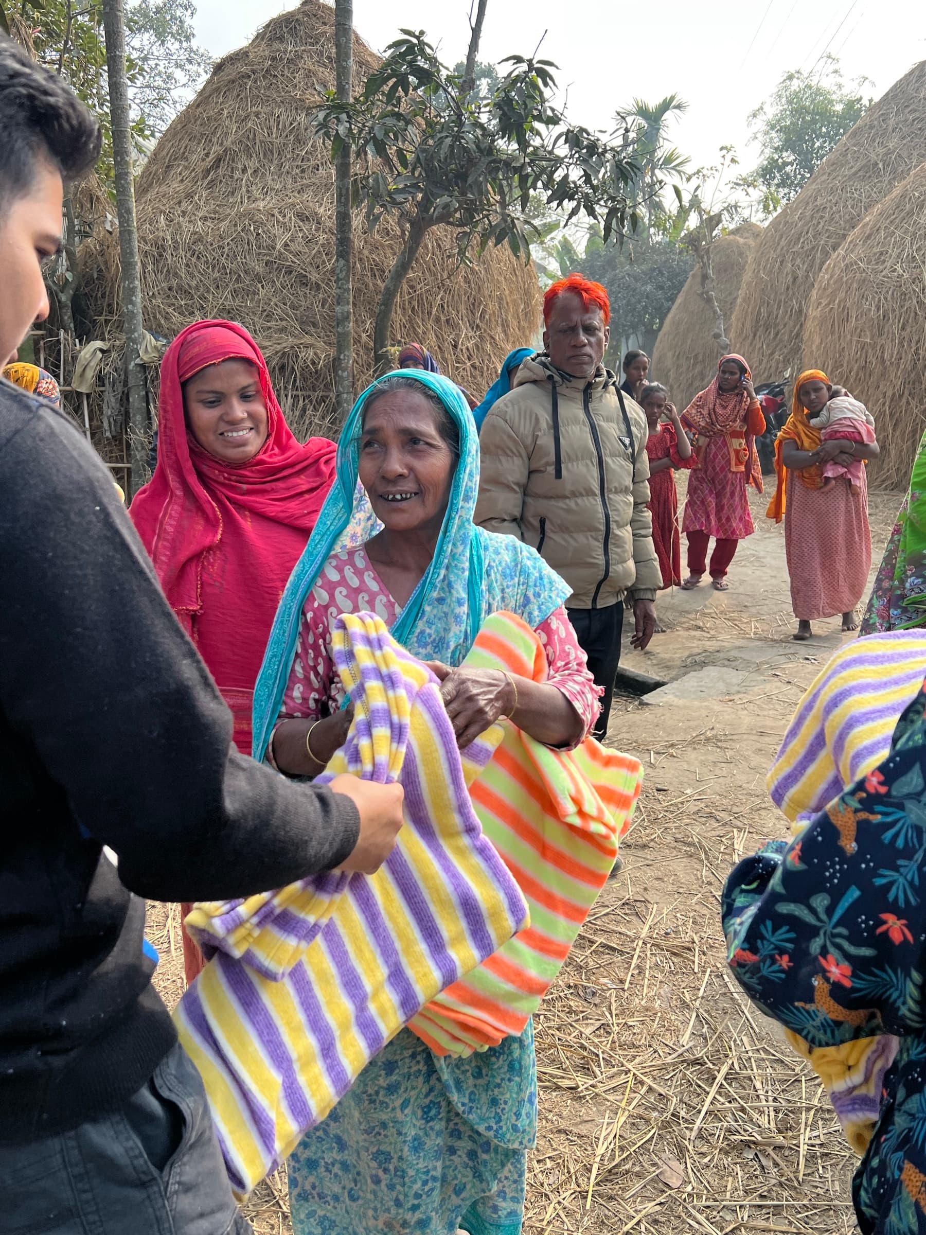 A volunteer handing a blanket to a woman in rural Rangpur